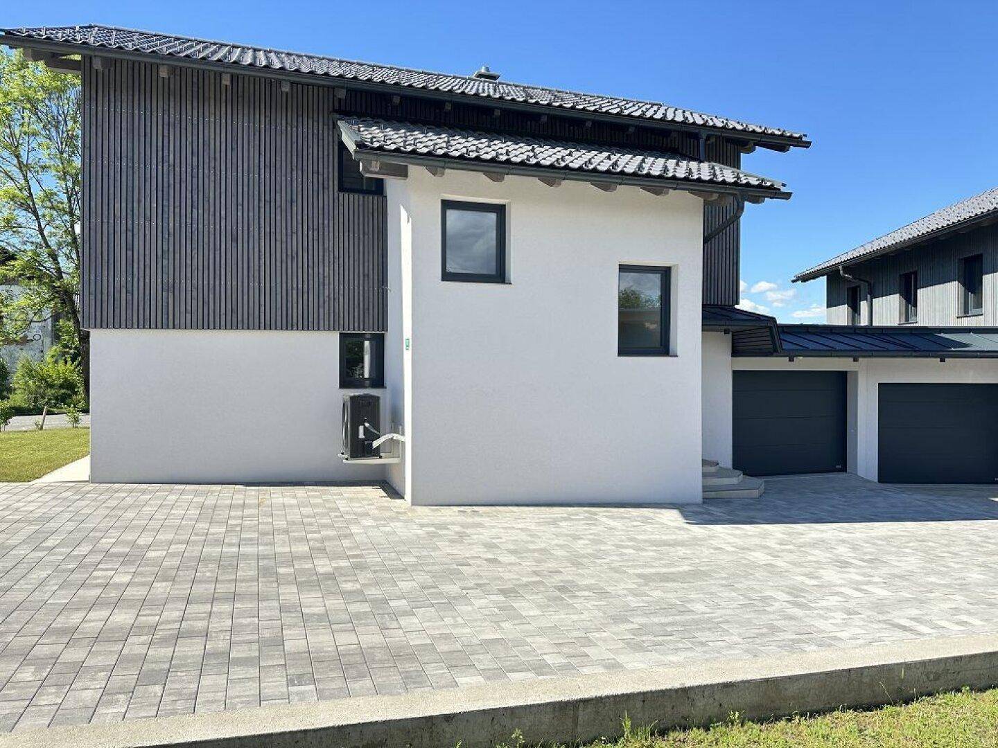 Seitenansicht des modernen Hauses mit gepflasterter Einfahrt und zwei Garagen.
