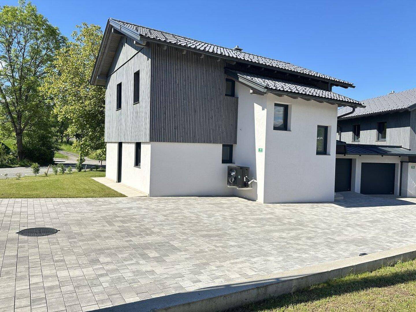 Modernes Haus mit Holzverkleidung und weißem Putz, umgeben von einer gepflasterten Fläche.