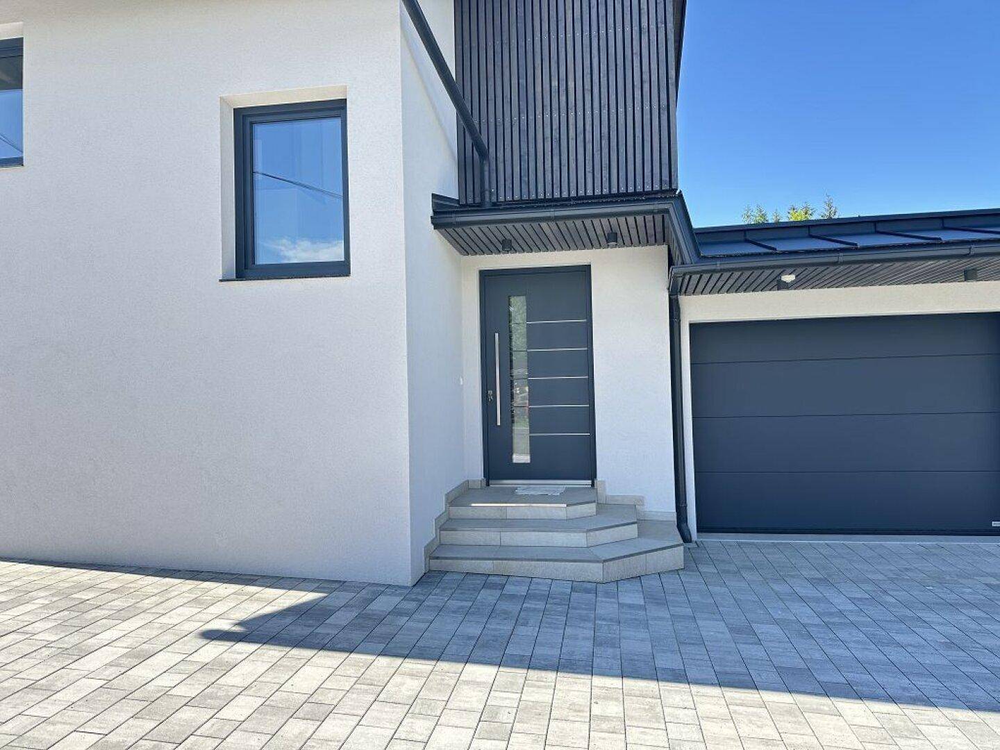 Moderner Hauseingang mit Treppe und angrenzender Garage, schlicht und funktional gestaltet.