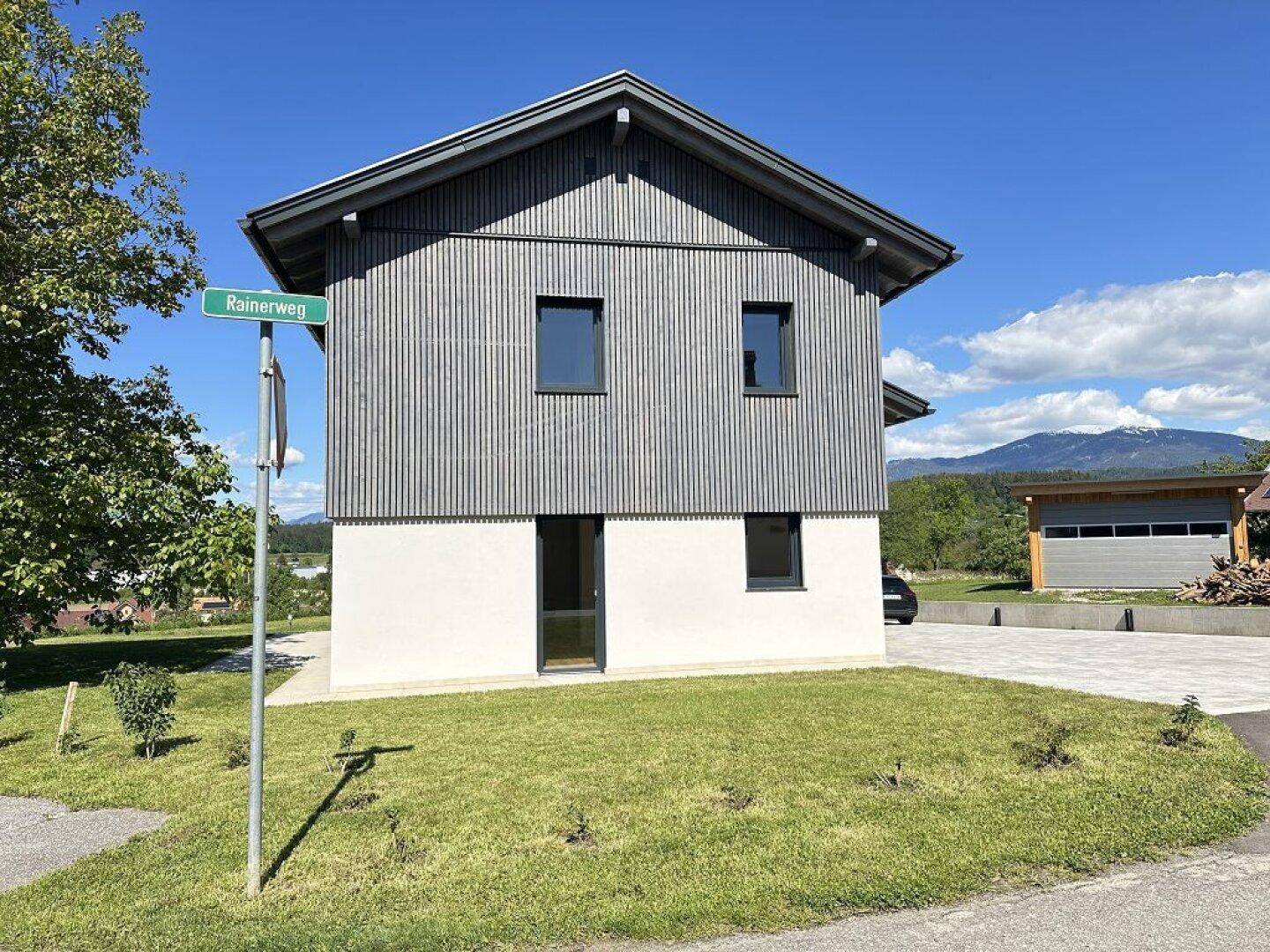 Vorderansicht des modernen Hauses mit Holzfassade und gepflegtem Vorgarten an der Straße.