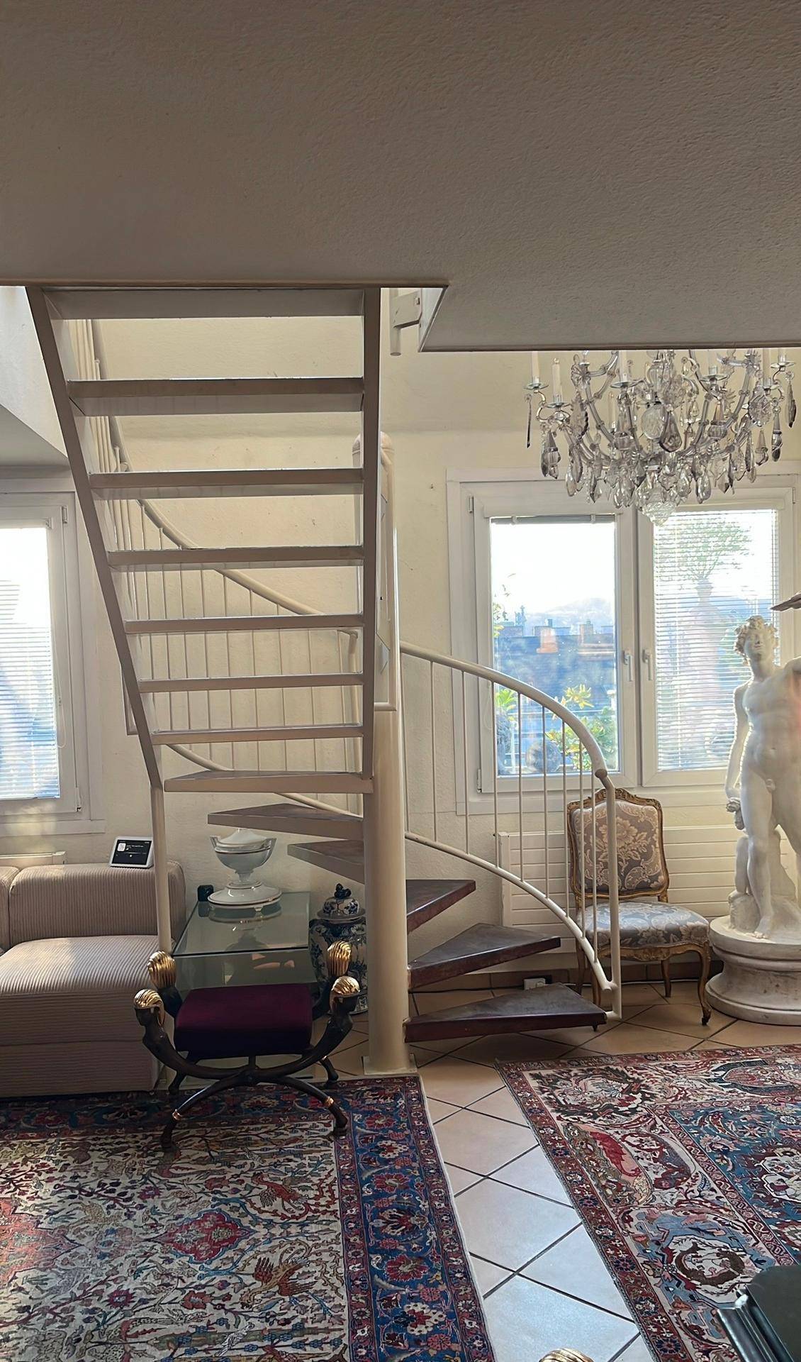 Helles Wohnzimmer mit zwei Treppen, darunter eine elegante Wendeltreppe, und großen Fenstern.