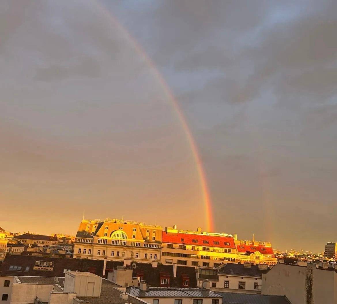 Malerischer Sonnenuntergang über der Stadt mit einem doppelten Regenbogen über den Dächern.