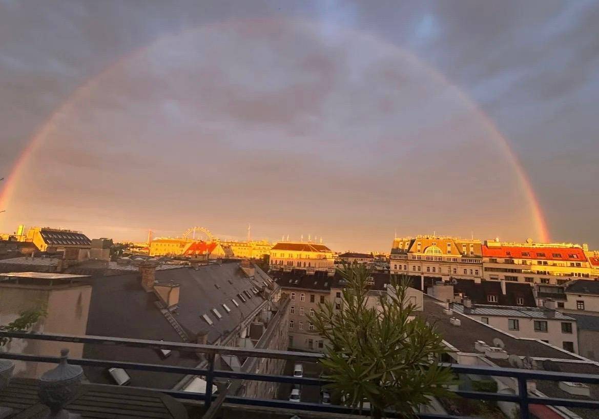 Spektakulärer Sonnenuntergang über der Stadt mit einem leuchtenden Regenbogen über den Dächern.