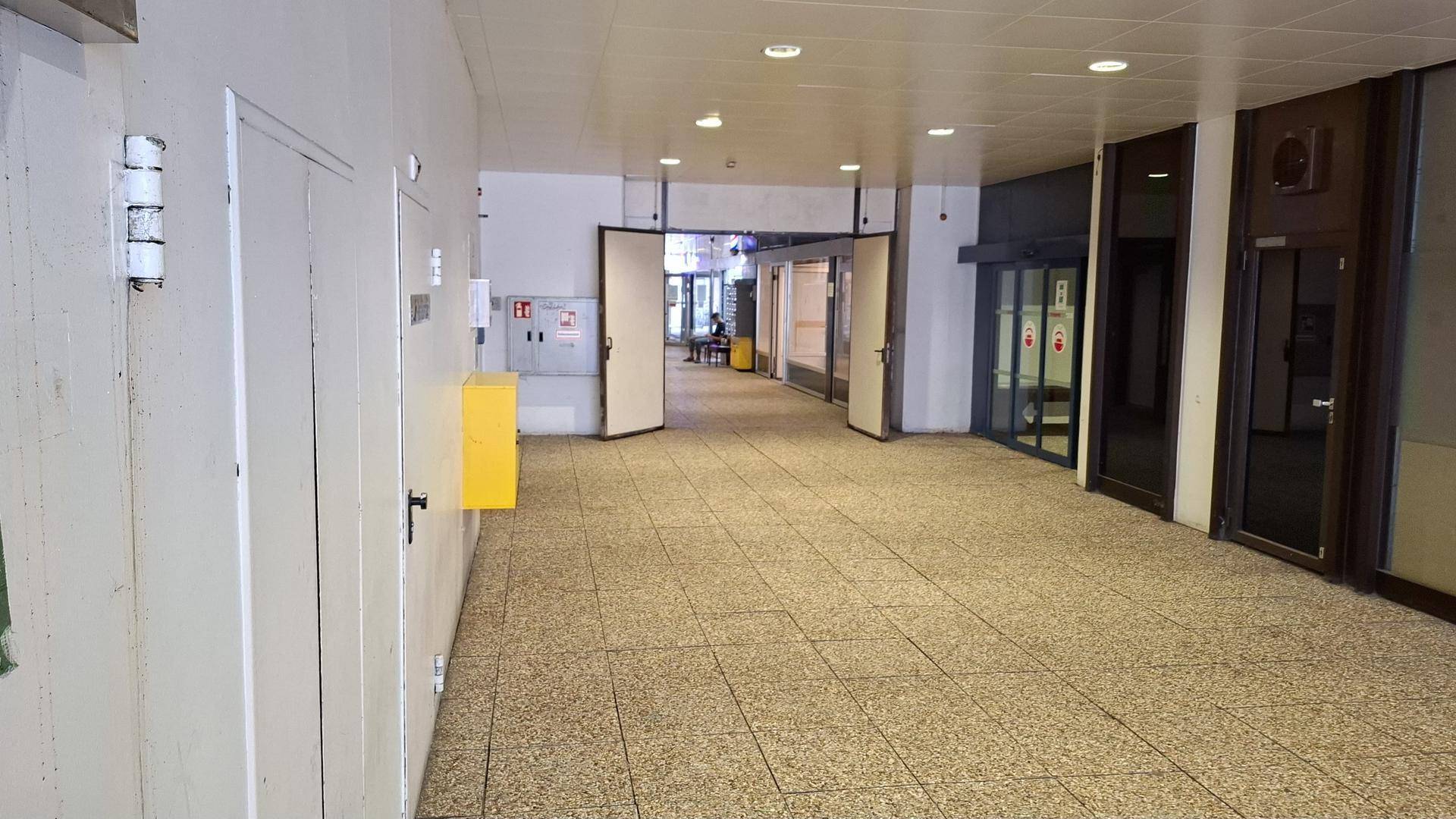 Breiter Innenflur mit Fliesenboden und mehreren Türen sowie Schaufenstern, die zu verschiedenen Einheiten führen.