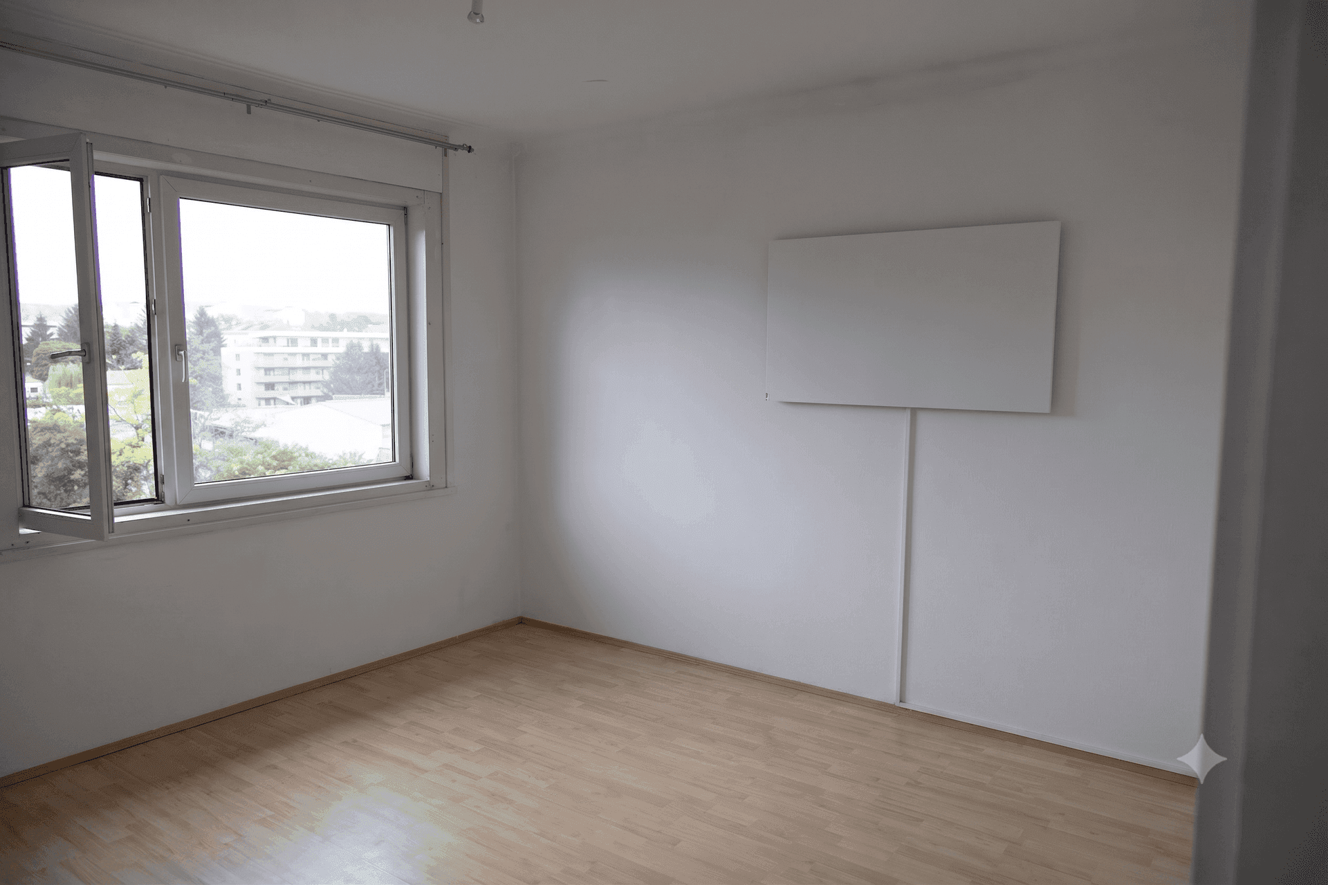 Heller Raum mit Holzboden, großem Fenster und einer Wandheizung, bietet viel Tageslicht.