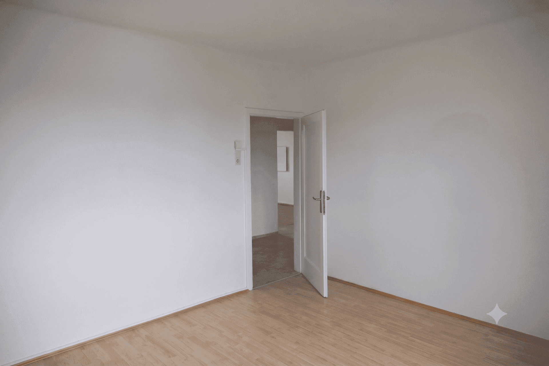 Leerer Raum mit Holzboden und einer offenen Tür, die den Blick in einen weiteren Bereich freigibt.