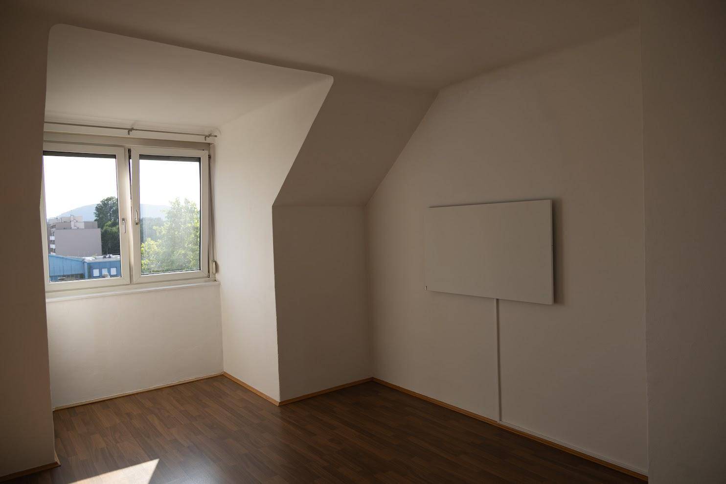Dachgeschosszimmer mit dunklem Holzboden, schrägen Wänden und einem Fenster mit Ausblick.