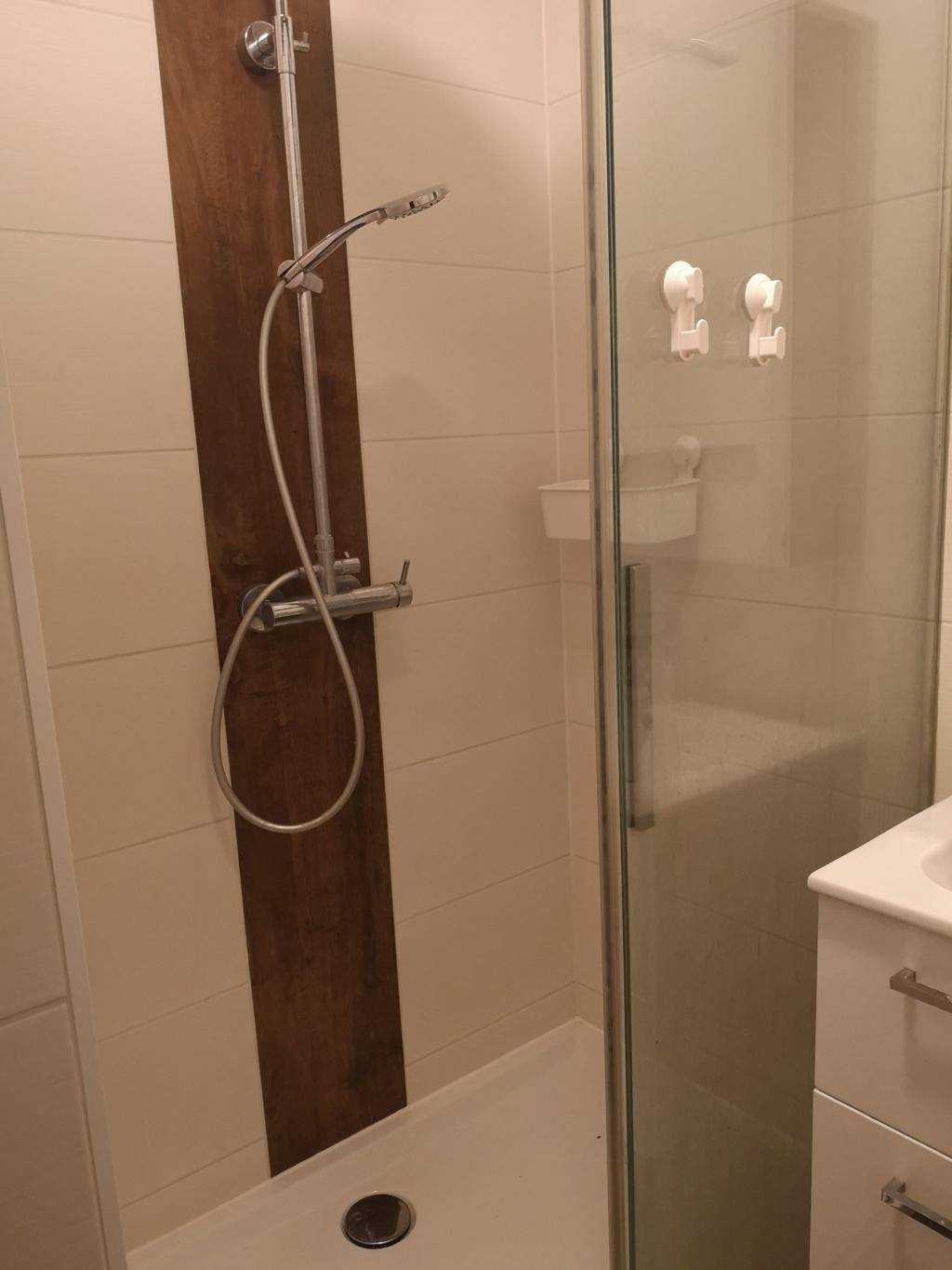 Moderne Dusche mit Glasabtrennung und Holzakzent an der Wand.