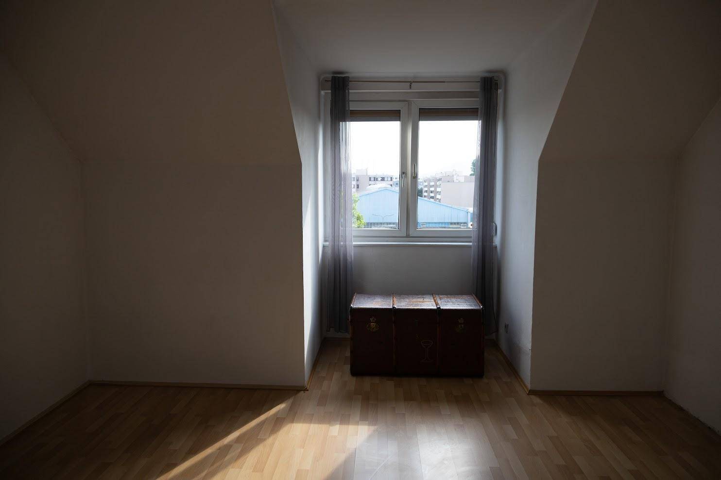 Dachgeschosszimmer mit Holzboden, schrägen Wänden und einem Fenster mit Blick nach draußen.