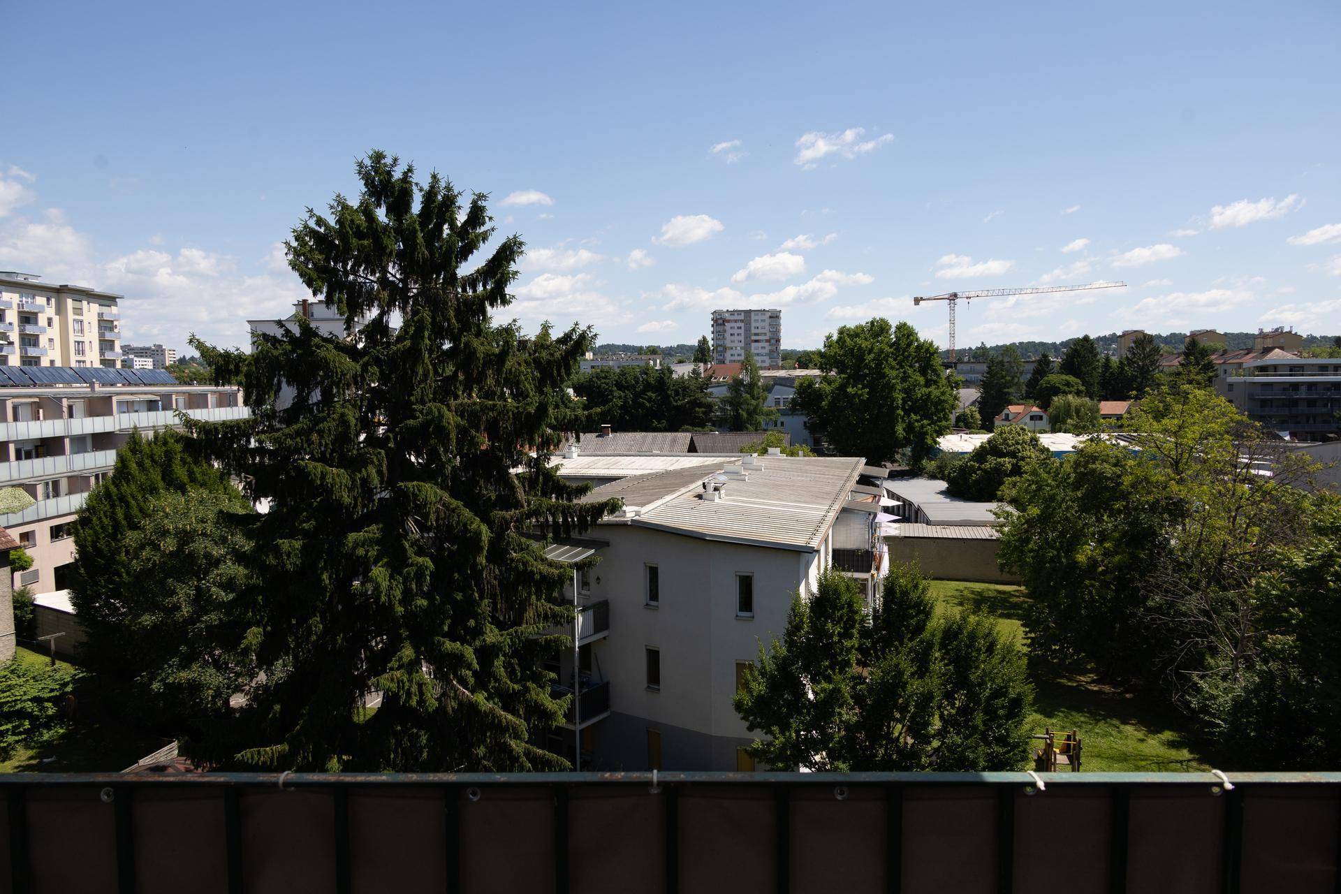 Weitblick über die Stadt mit viel Grün und umliegenden Gebäuden von einem Balkon.