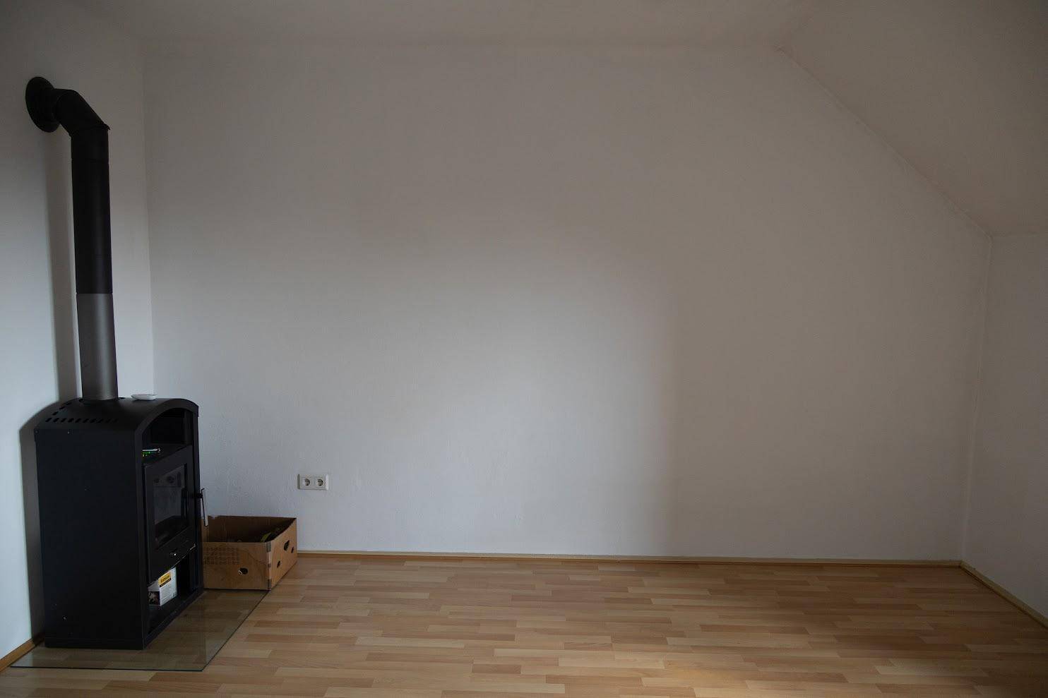 Heller Raum mit Kaminofen und Holzboden, bereit zur individuellen Gestaltung.