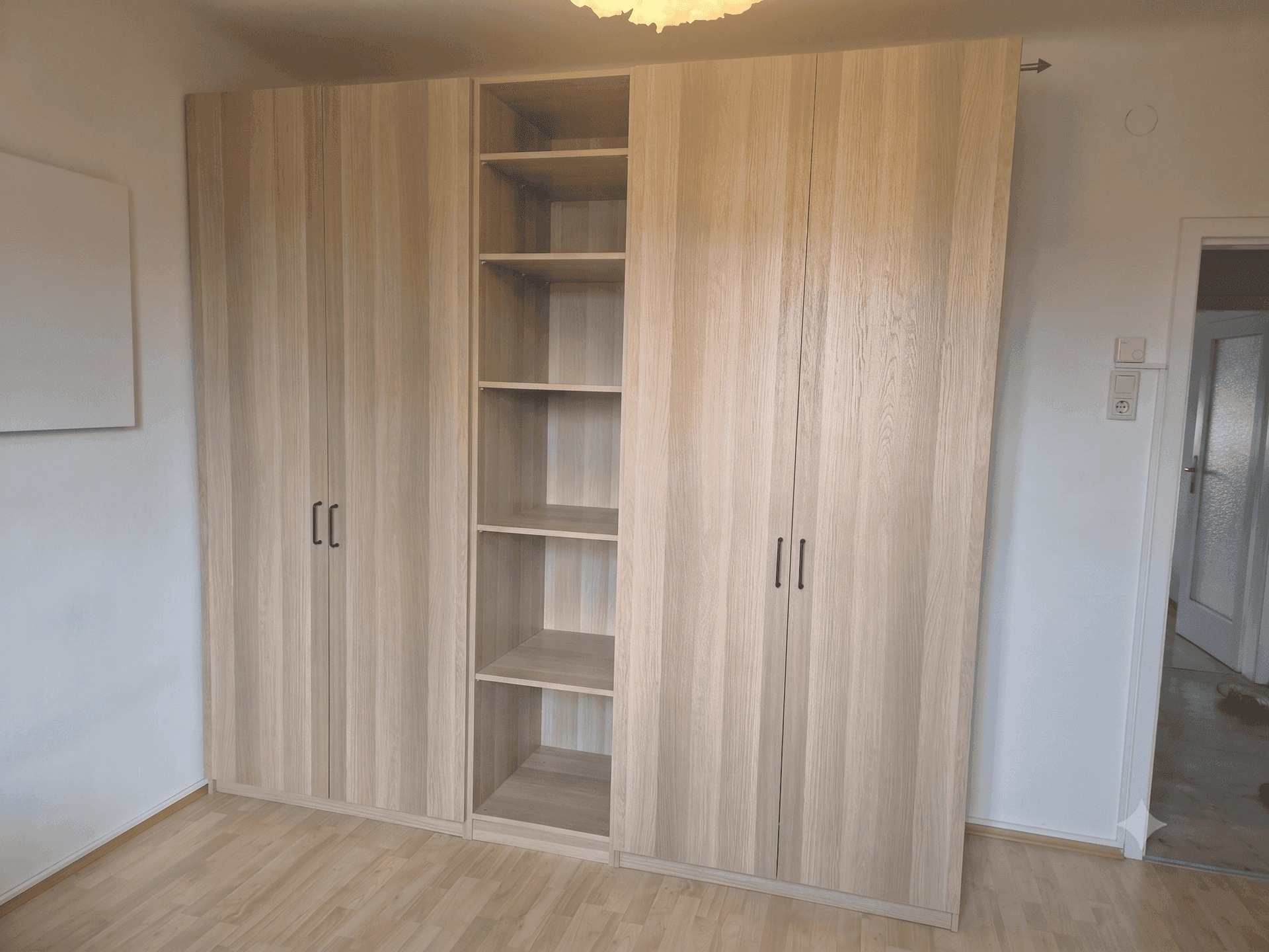Schlafzimmer mit hellem Holzboden und einem großen Einbauschrank mit offenen Regalfächern.