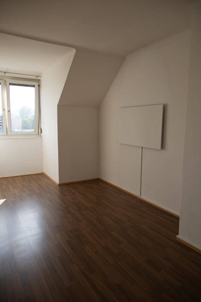 Helles Dachgeschosszimmer mit dunklem Holzboden, schrägen Wänden und einem großen Fenster.