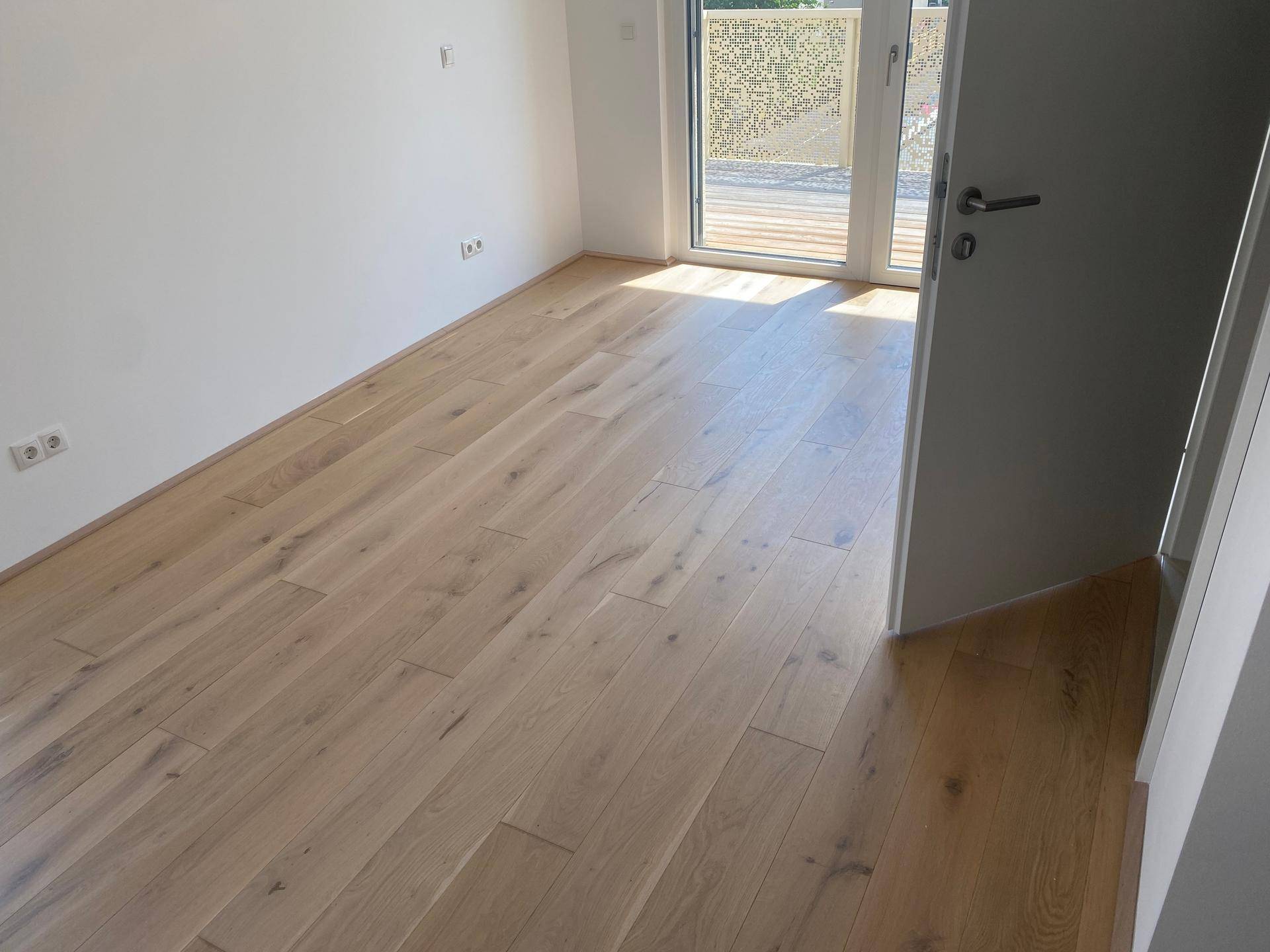 Helles Zimmer mit Parkettboden und Zugang zu einem Außenbereich, durchflutet von Sonnenlicht.