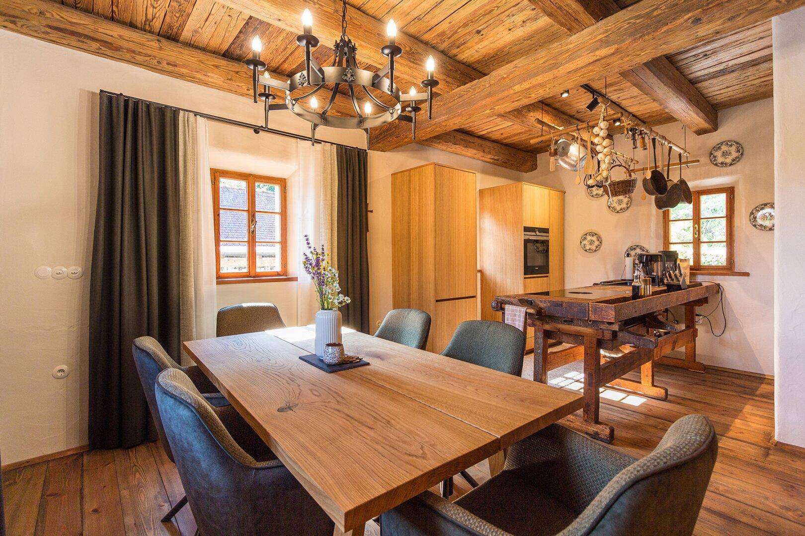 Rustikaler Essbereich mit großem Holztisch, Holzbalkendecke und integrierter Küchenzeile.