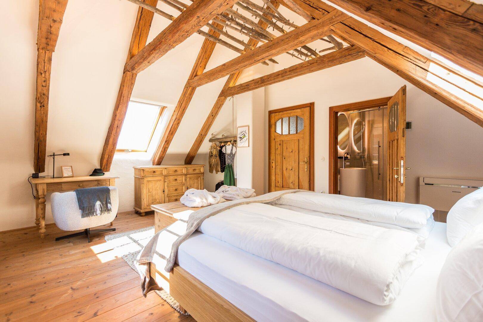 Helles Schlafzimmer im Dachgeschoss mit Holzbalken, Holzboden und Schreibtisch.