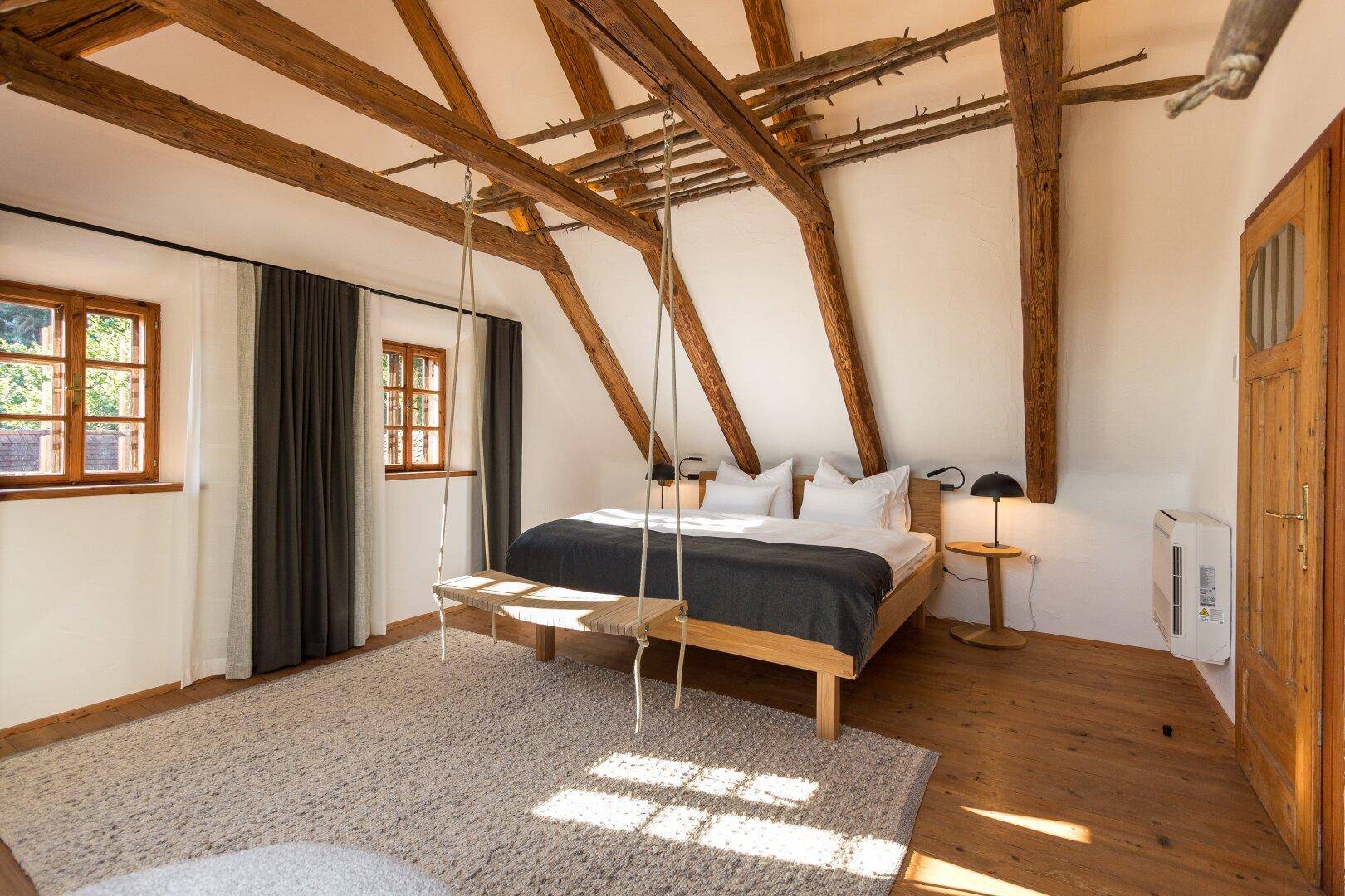 Charmantes Schlafzimmer mit Holzbalken, Holzboden und einer Schaukel für entspannte Momente.