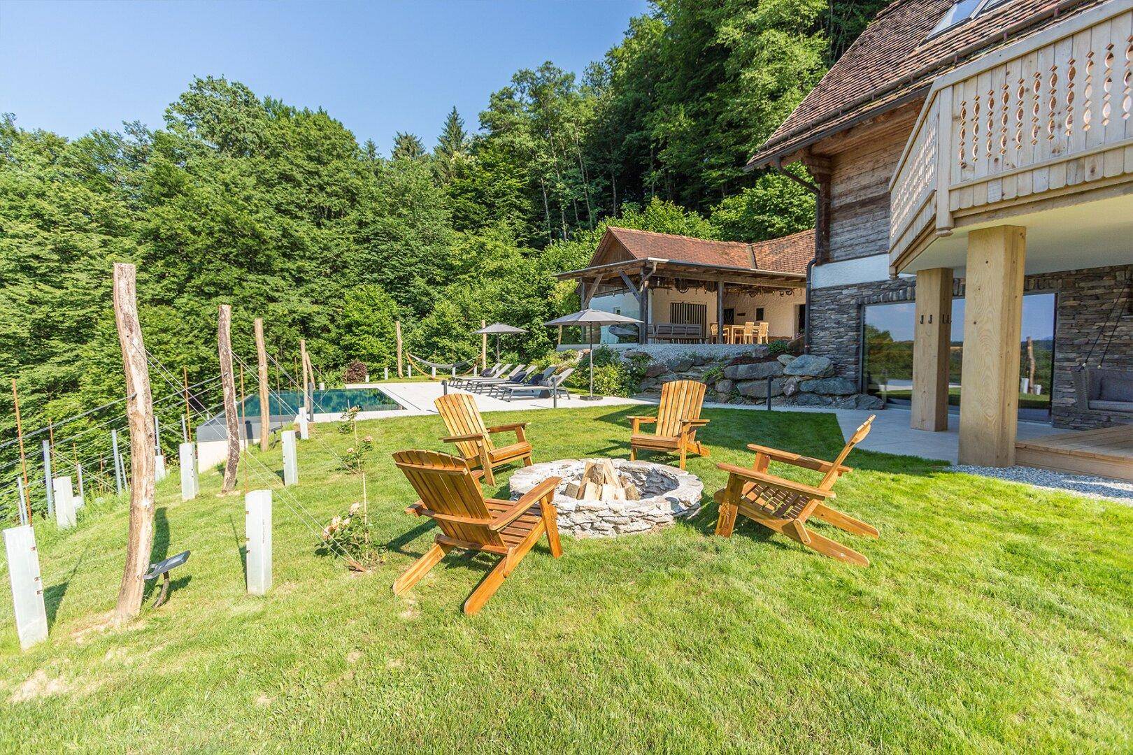 Großer Gartenbereich mit Feuerstelle, Holzstühlen und Blick auf den Pool und die Weinberge.