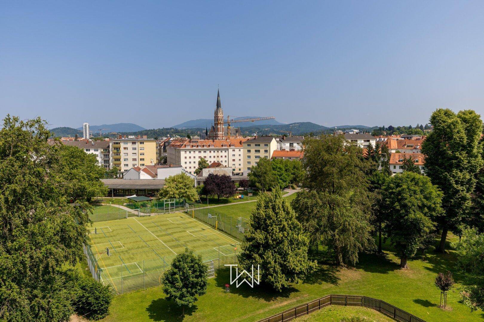 Weitläufiger Blick über die Stadt mit grünen Sportanlagen und Wohngebäuden.