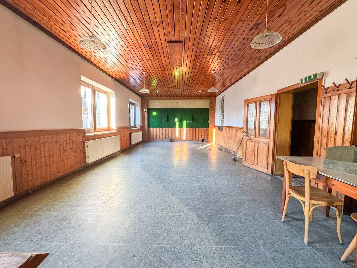Langer Raum mit Holzdecke und -vertäfelung, hell durch Fenster, bereit für Renovierung.
