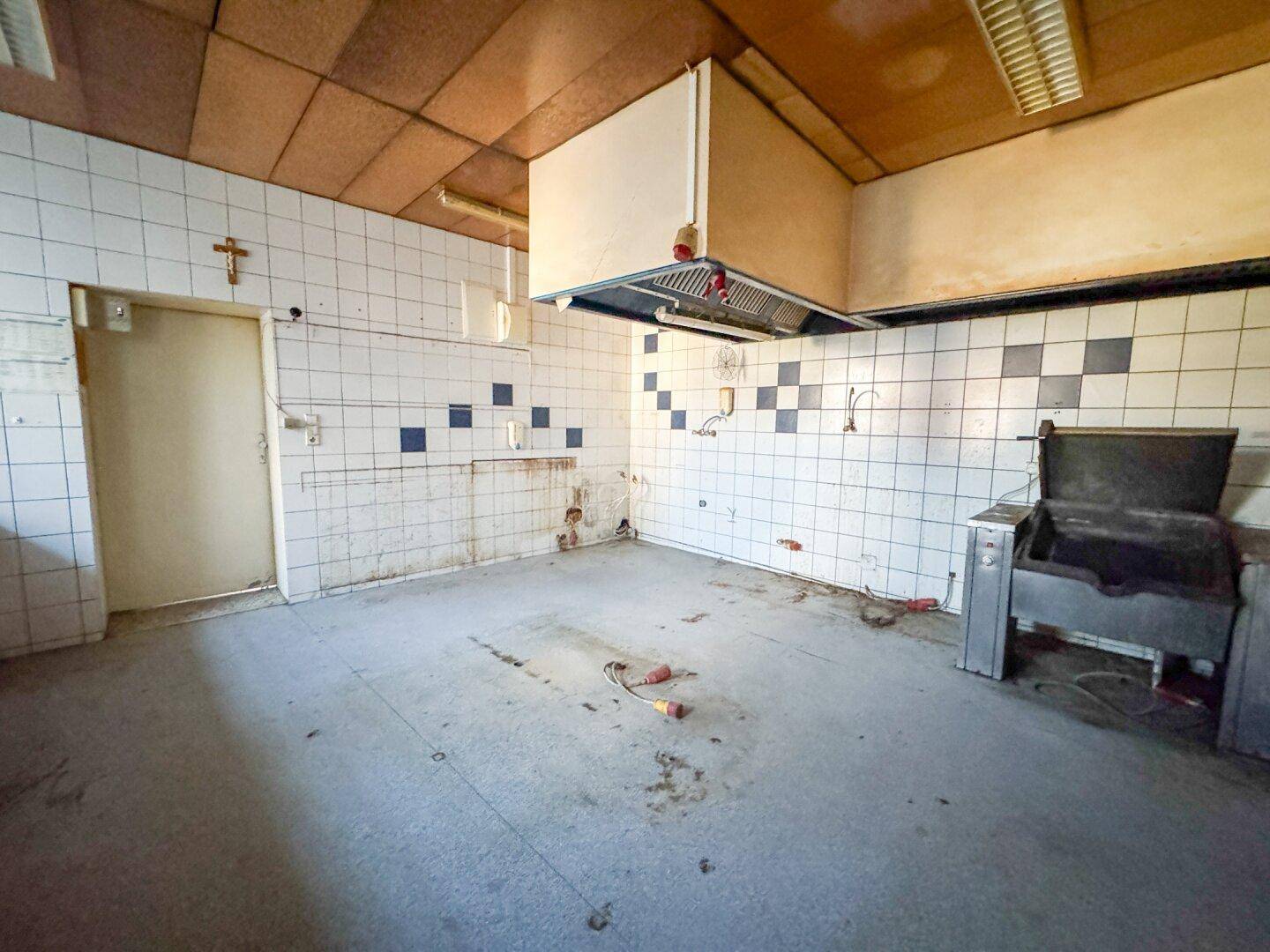 Leere Küche mit alten Fliesen und Dunstabzugshaube, benötigt umfassende Renovierung.