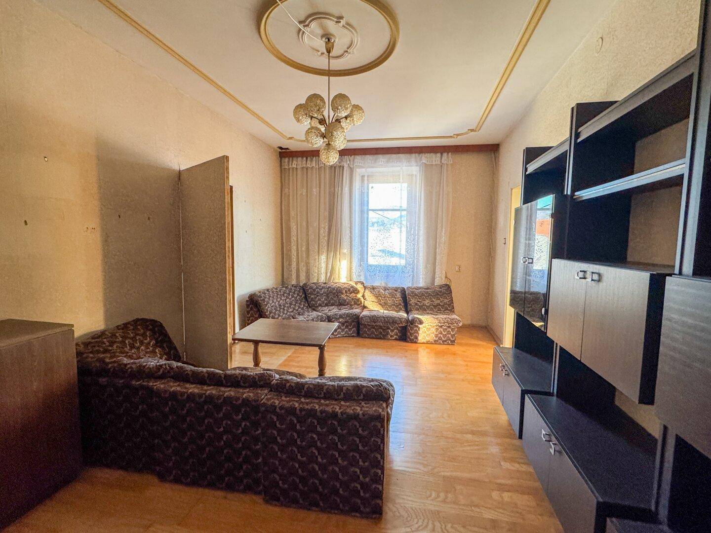 Helles Wohnzimmer mit Parkettboden, Stuckdecke und Vintage-Möbeln, wartet auf Modernisierung.