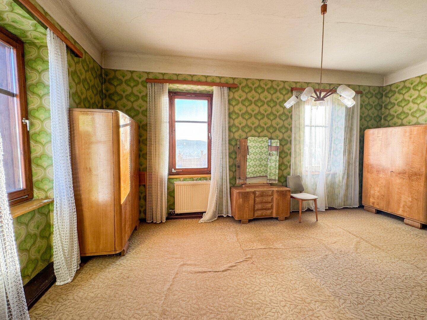 Schlafzimmer mit gemusterter Tapete, Teppichboden und Vintage-Möbeln, bietet viel Potenzial.
