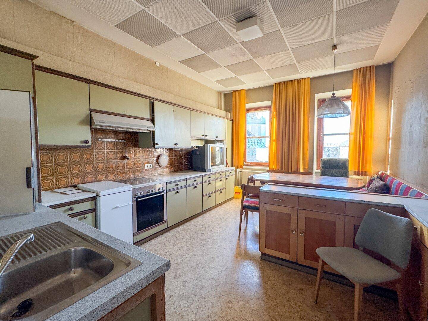 Ältere Wohnküche mit Einbauschränken, Geräten und Essbereich, benötigt Modernisierung.