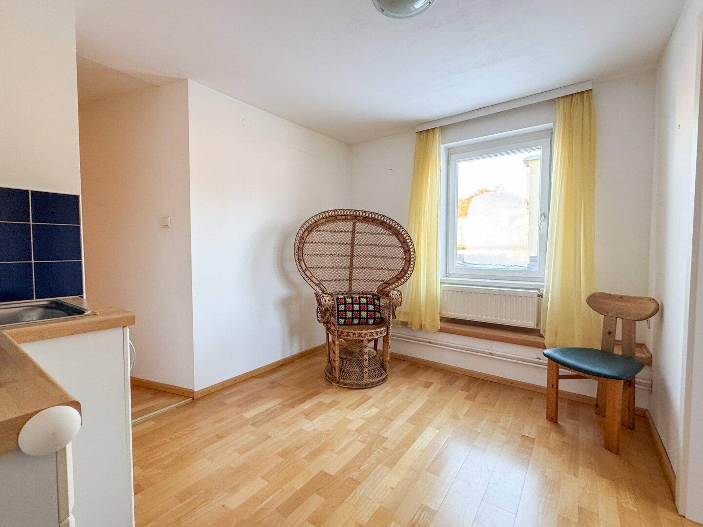Heller Raum mit Parkettboden und kleiner Küchenzeile, ideal für ein Studio-Apartment.