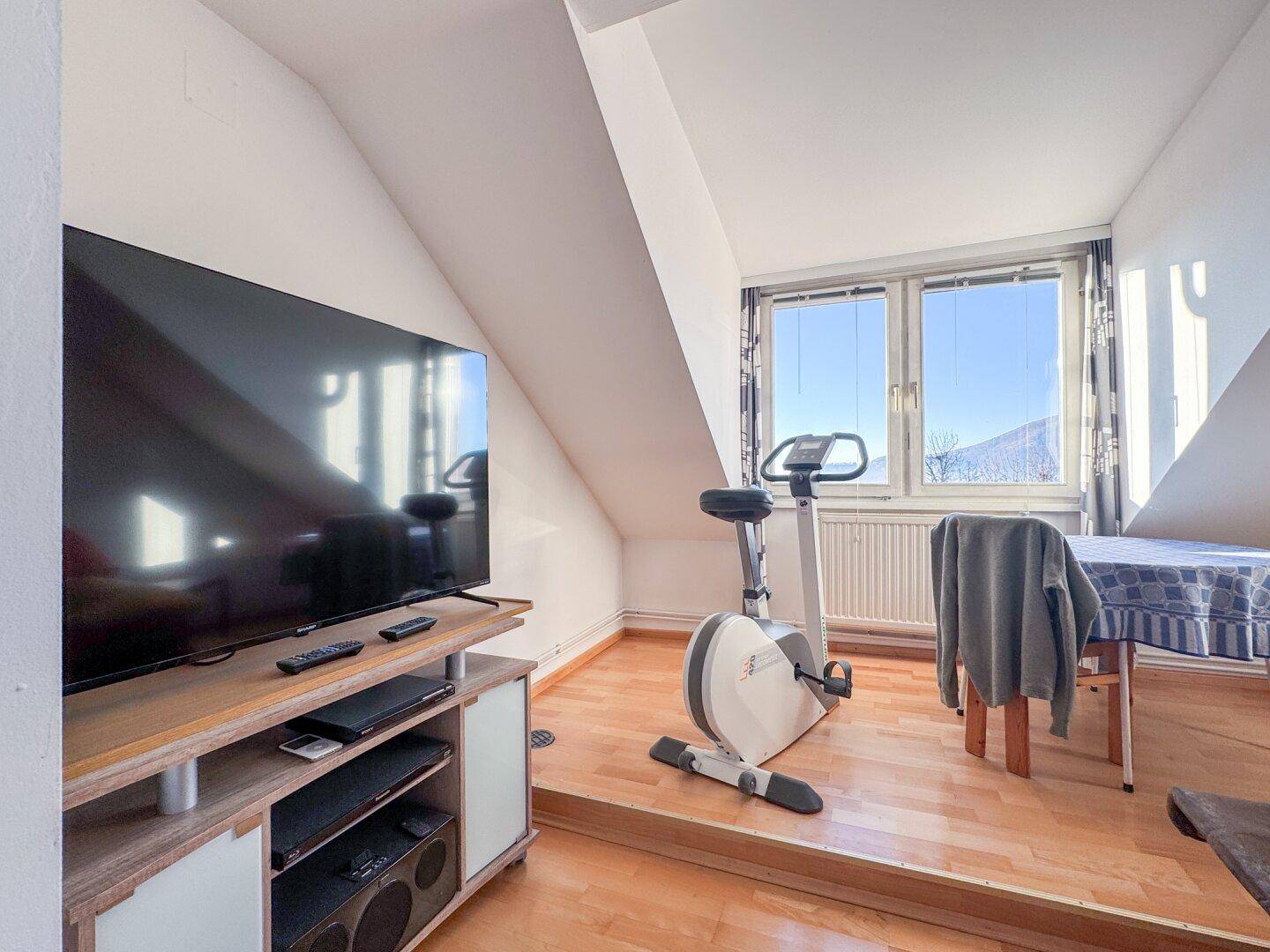 Helles Dachgeschosszimmer mit Holzboden, schrägen Wänden und Blick auf die Berge.