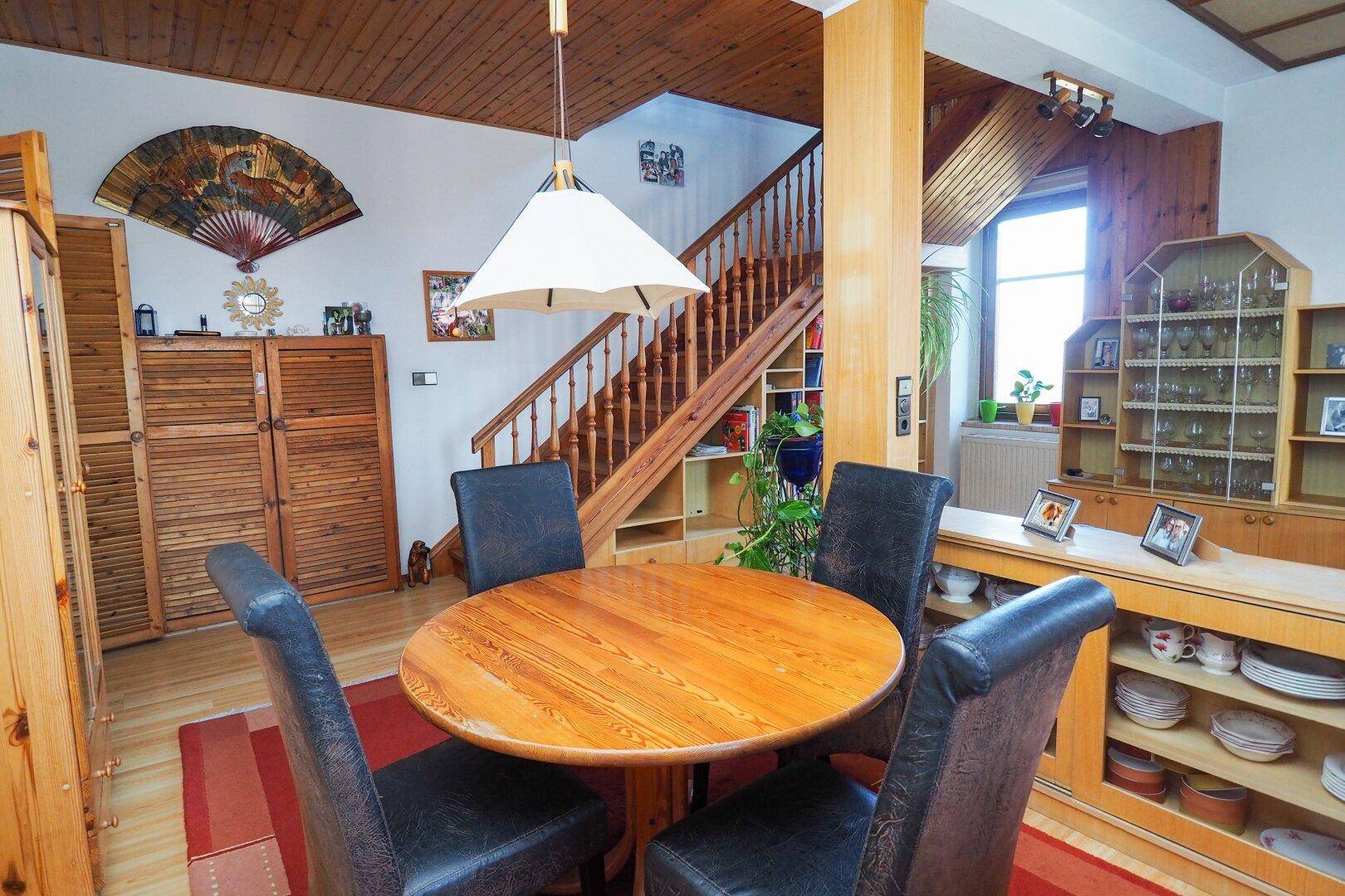 Gemütlicher Essbereich mit rundem Holztisch und Holztreppe, schafft eine warme Atmosphäre.