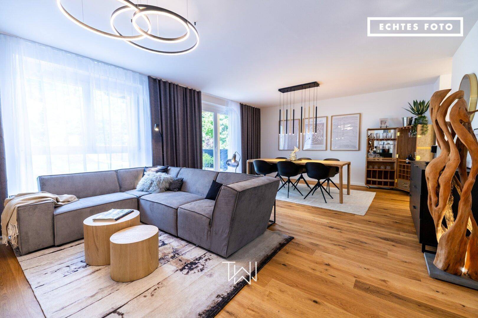 Heller, offener Wohn- und Essbereich mit modernem Sofa, Holzboden und großen Fenstern.