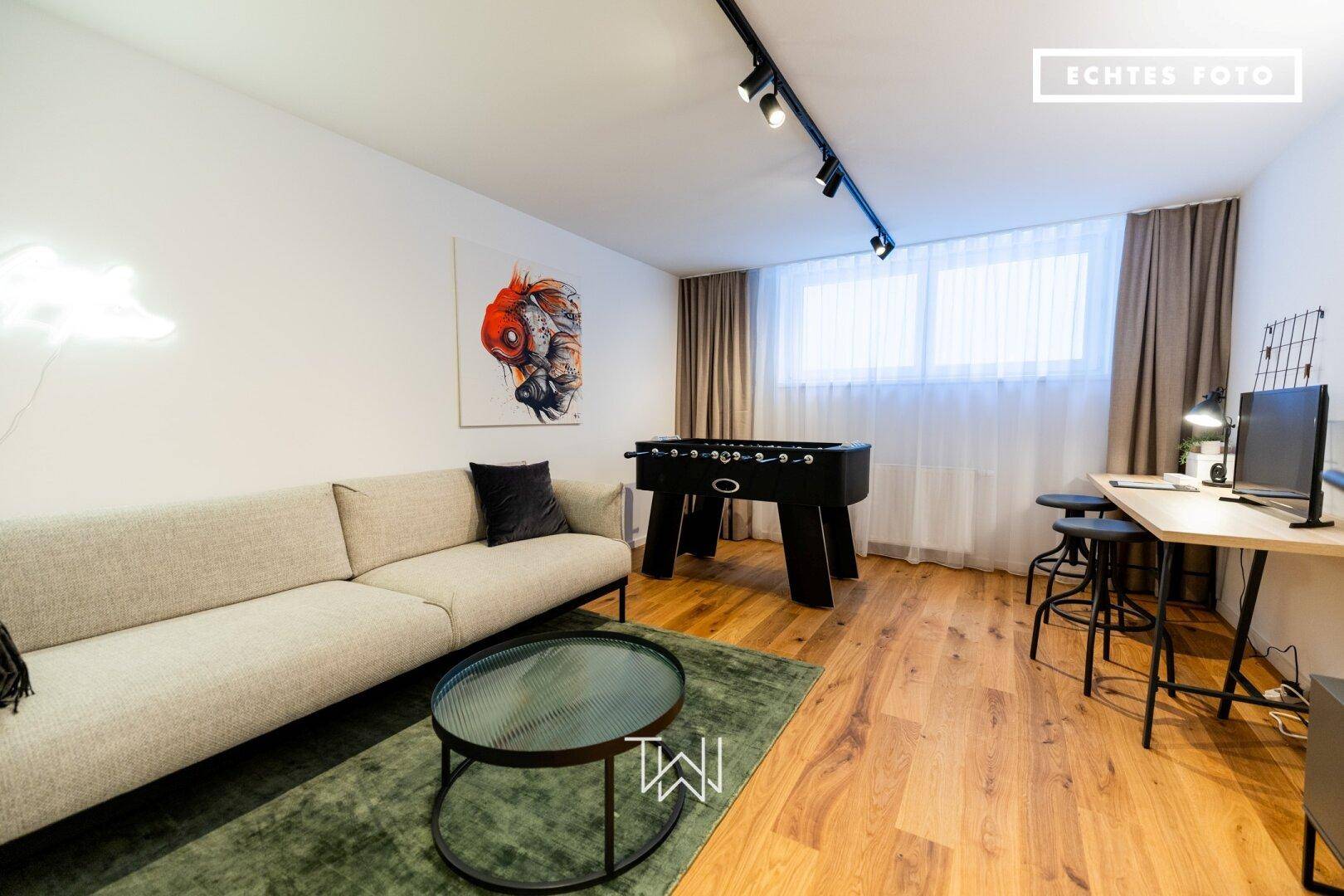Gemütlicher Wohnbereich mit Sofa, Tischkicker und Arbeitsplatz, ideal für Freizeit und Arbeit.