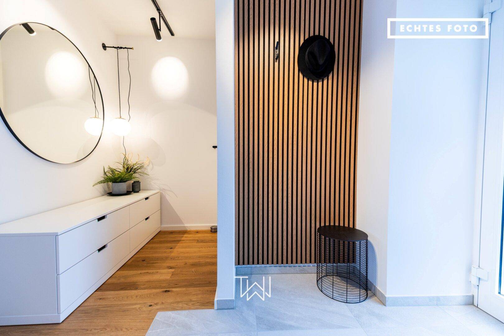 Moderner Flur mit Holzlamellenwand, großem Spiegel und Holzboden.
