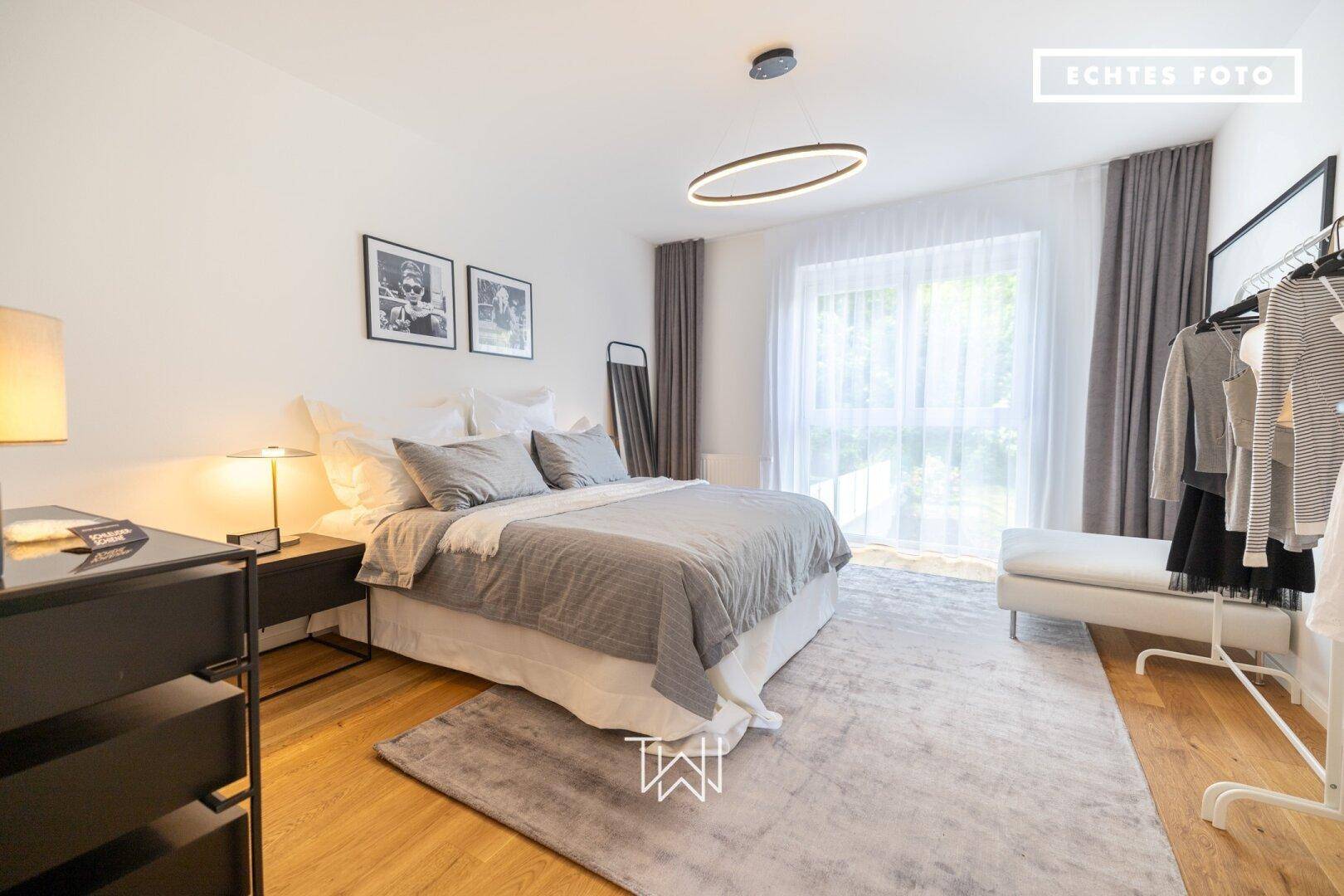 Modernes Schlafzimmer mit großem Bett, Holzboden und Zugang zu einem Balkon.