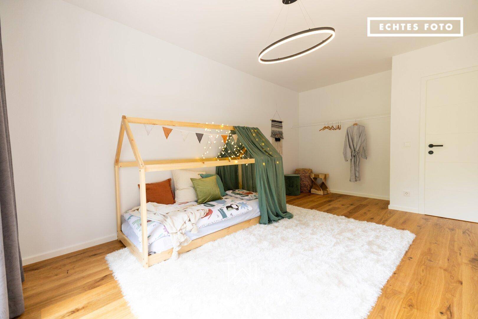 Helles Kinderzimmer mit Holzboden, Spielbett und minimalistischer Dekoration.