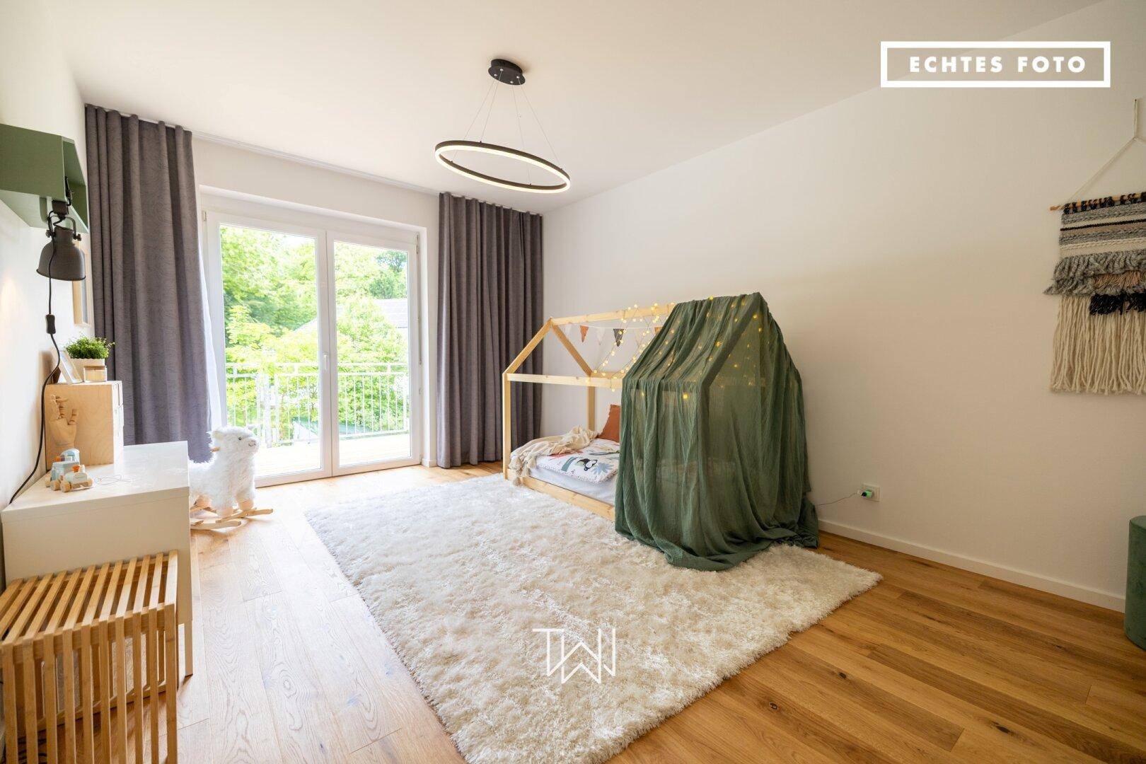 Freundliches Kinderzimmer mit Holzboden, Spielbett und Zugang zu einem Balkon.