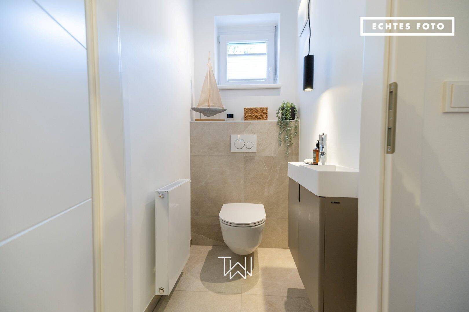 Modernes Gäste-WC mit Wand-WC, kleinem Waschbecken und Fenster für Tageslicht.