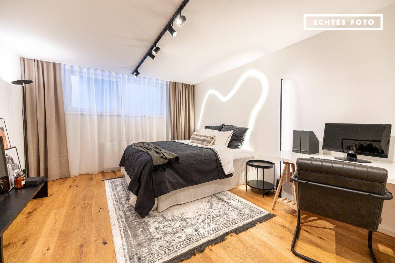 Modernes Schlafzimmer mit Holzboden, großem Bett und integriertem Arbeitsbereich.