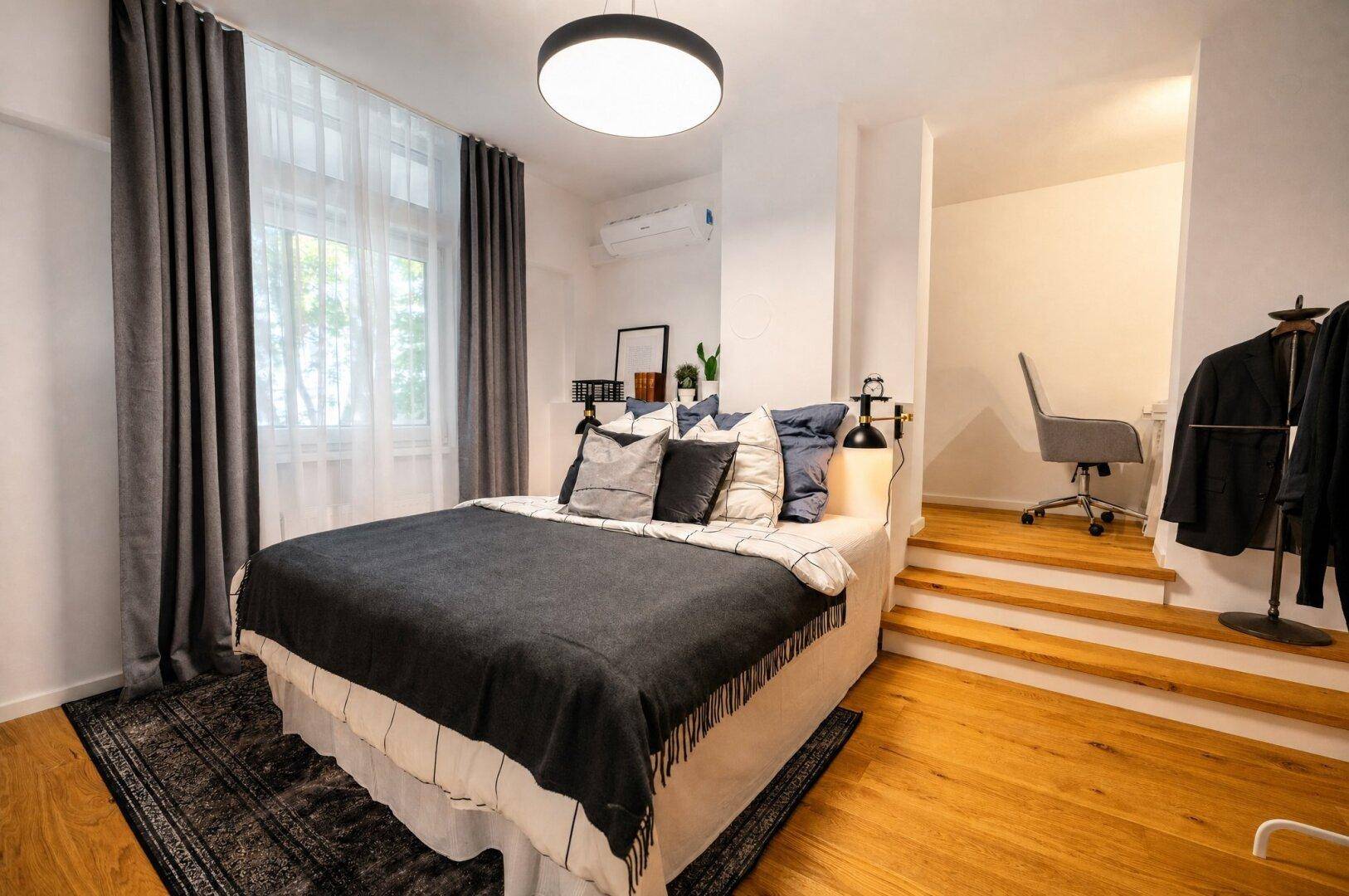 Schlafzimmer mit Doppelbett, dunklen Vorhängen und erhöhtem Arbeitsbereich.