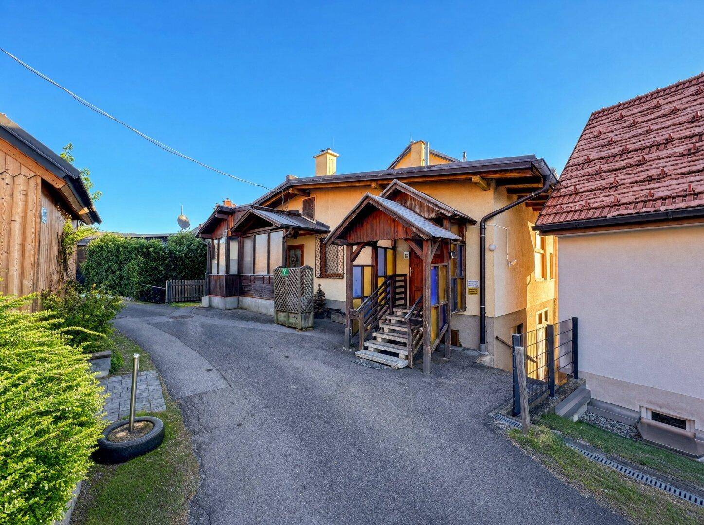 Seitenansicht eines Gebäudes mit Holzelementen, bunten Fenstern und einem gepflasterten Weg.