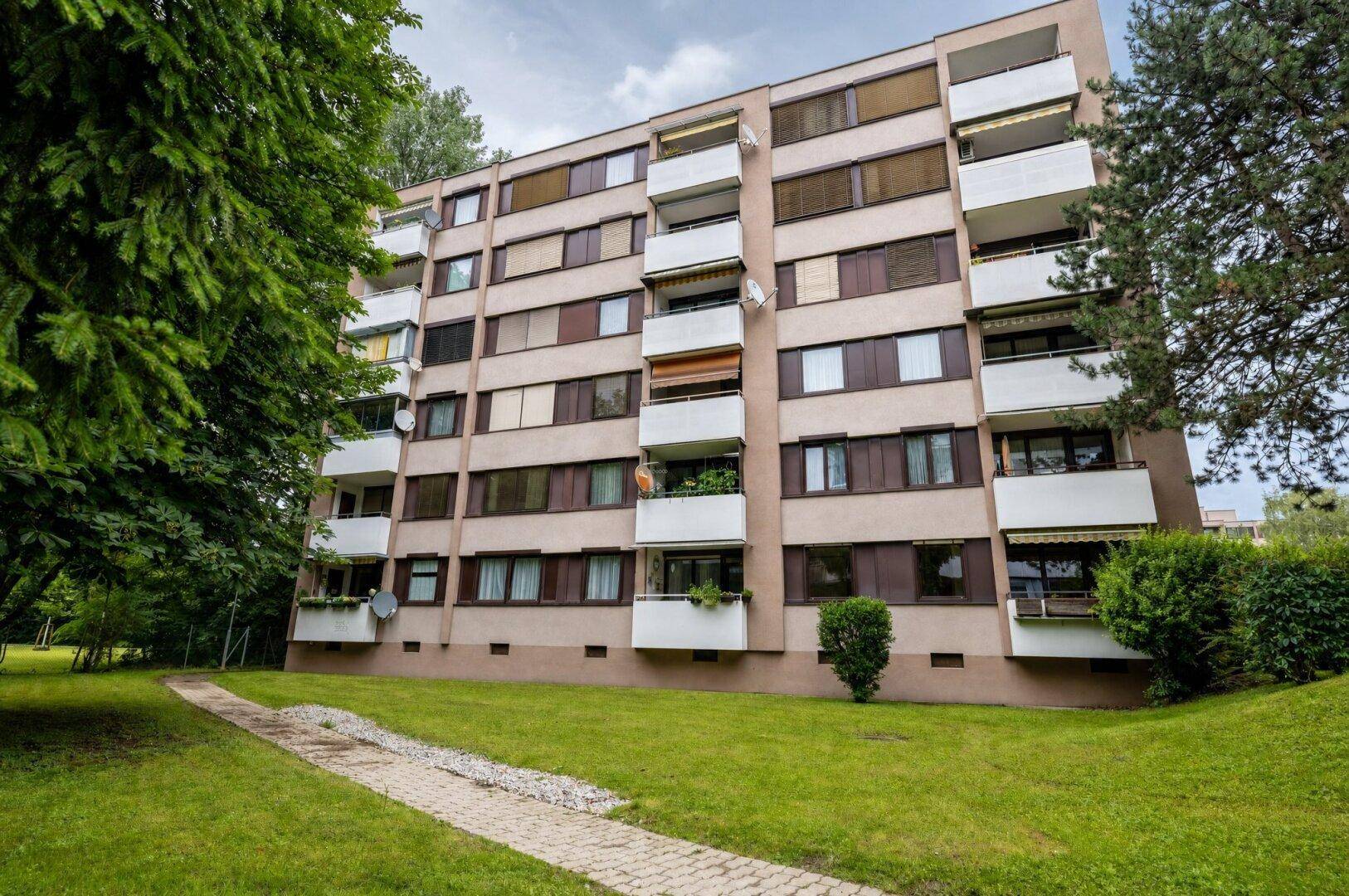Mehrfamilienhaus mit mehreren Balkonen und grüner Umgebung.