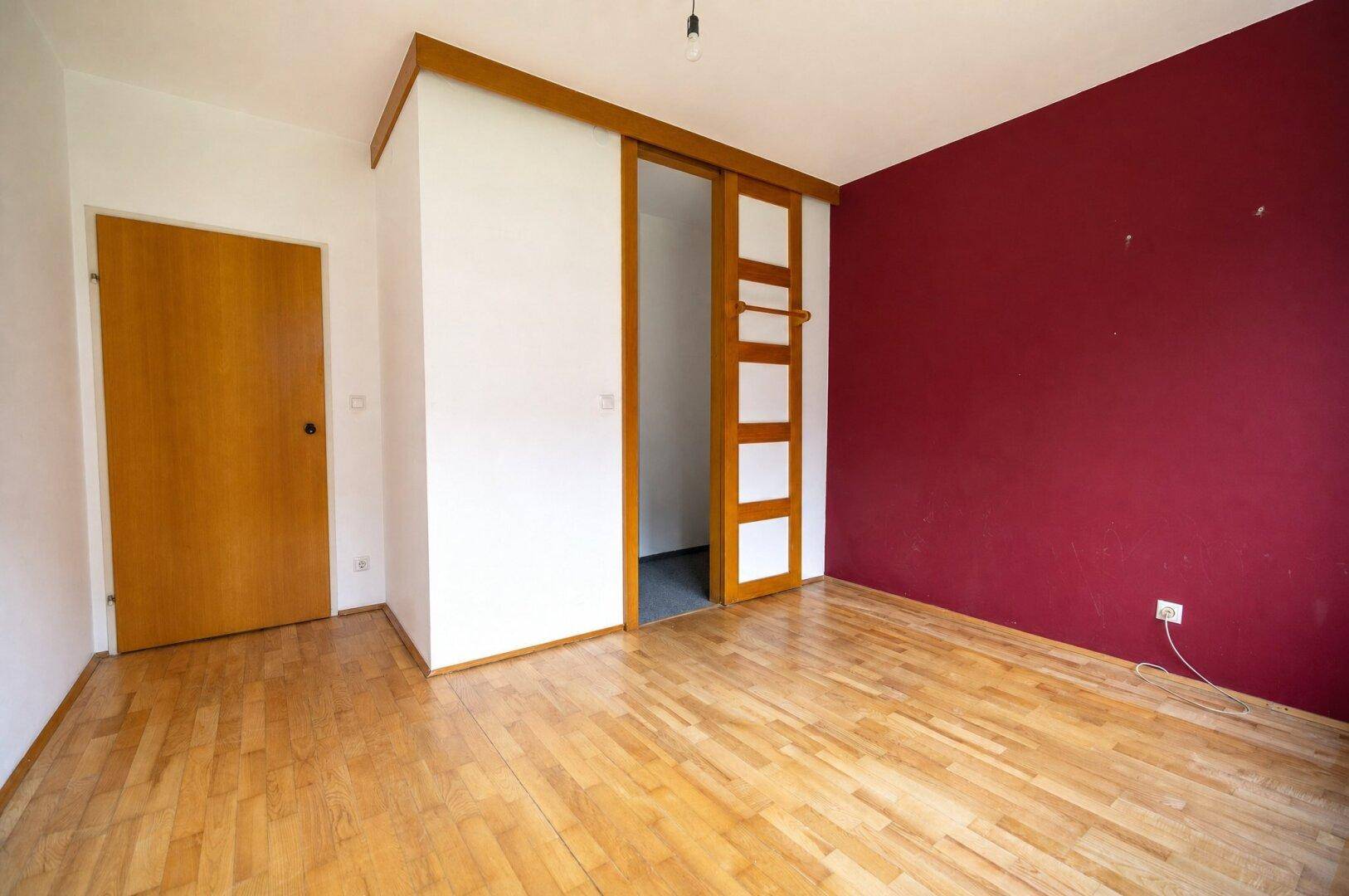 Schlafzimmer mit Parkettboden und einer Akzentwand in kräftigem Rot.