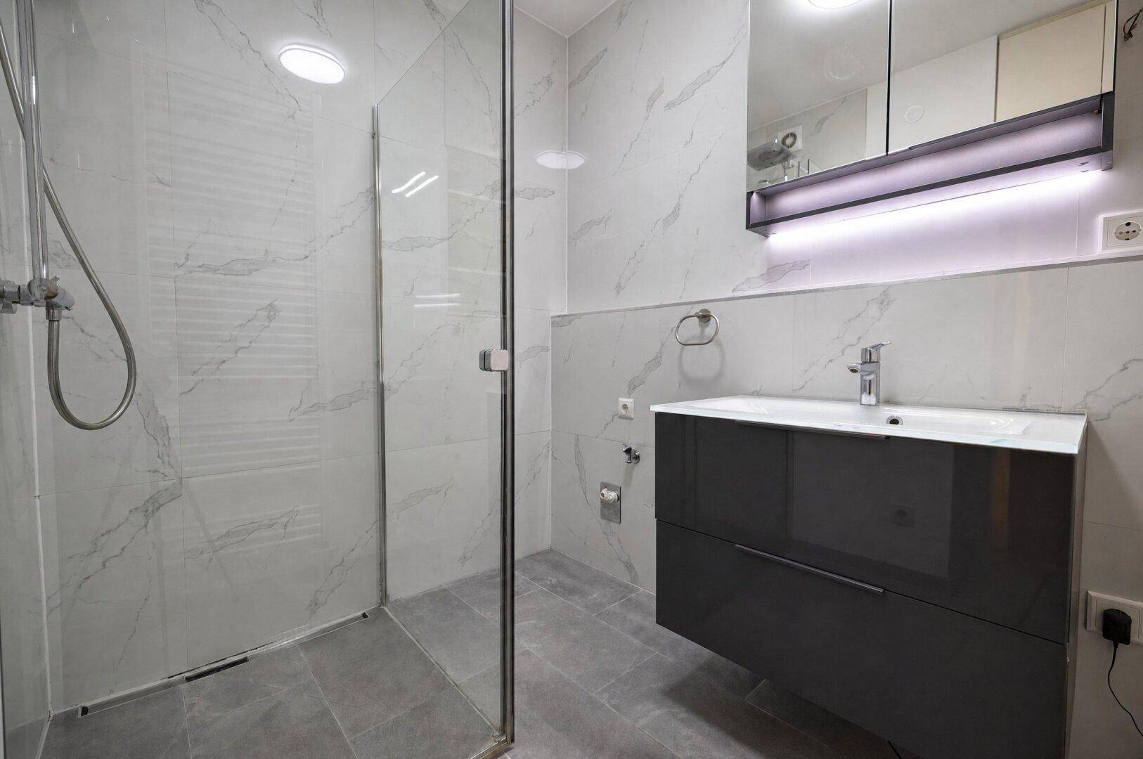 Modernes Badezimmer mit großer Dusche, Waschtisch und Spiegelschrank.