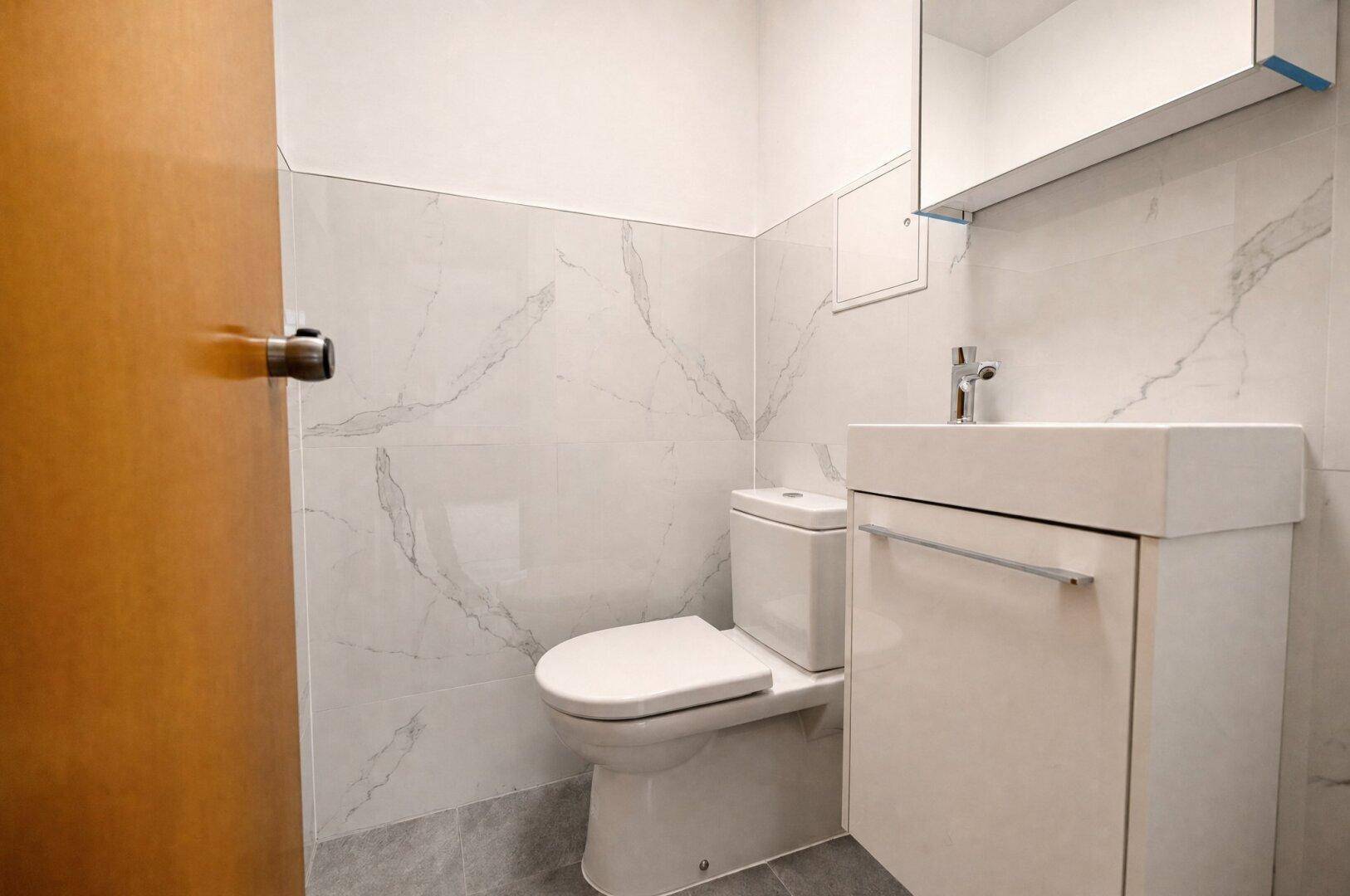 Separates WC mit modernem Waschtisch und Wandfliesen in Marmoroptik.