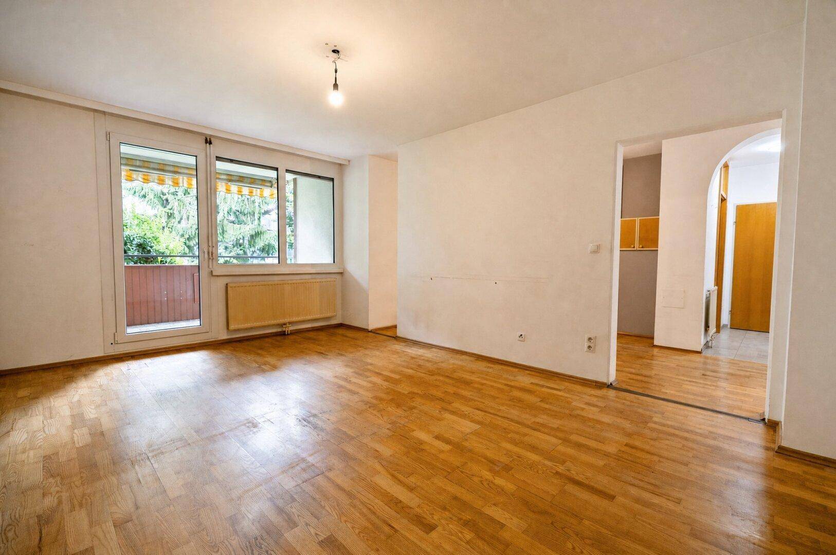 Geräumiges Wohnzimmer mit Parkettboden und Zugang zum Balkon.
