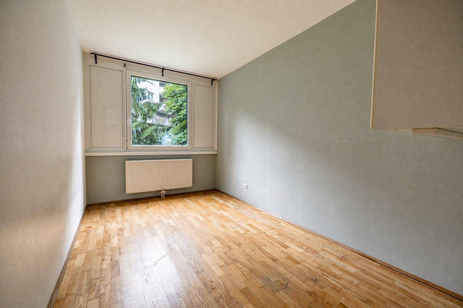 Helles Schlafzimmer mit Parkettboden und Fenster mit Blick ins Grüne.