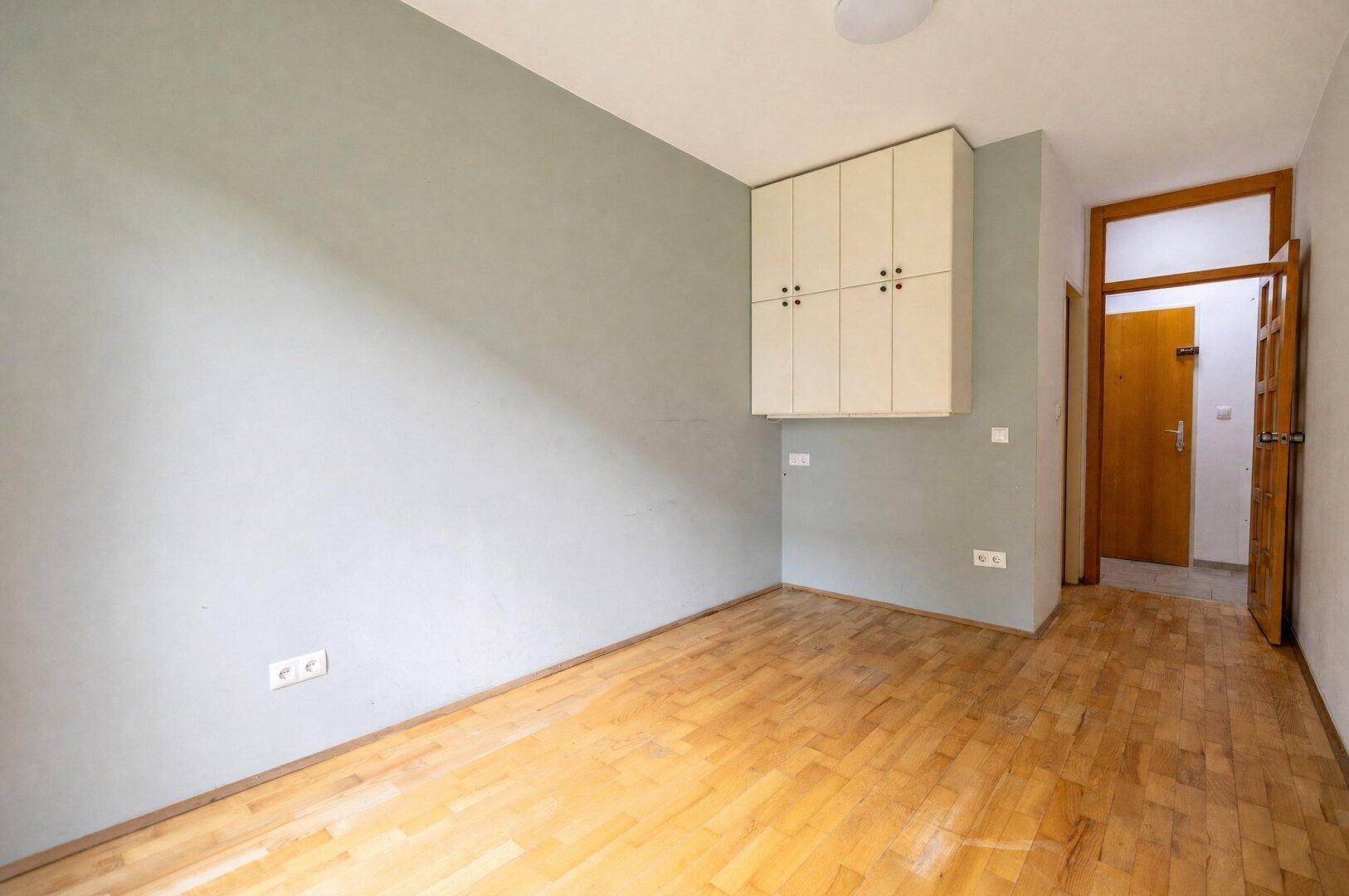 Schlafzimmer mit Parkettboden und Wandschrank, Zugang zum Flur.