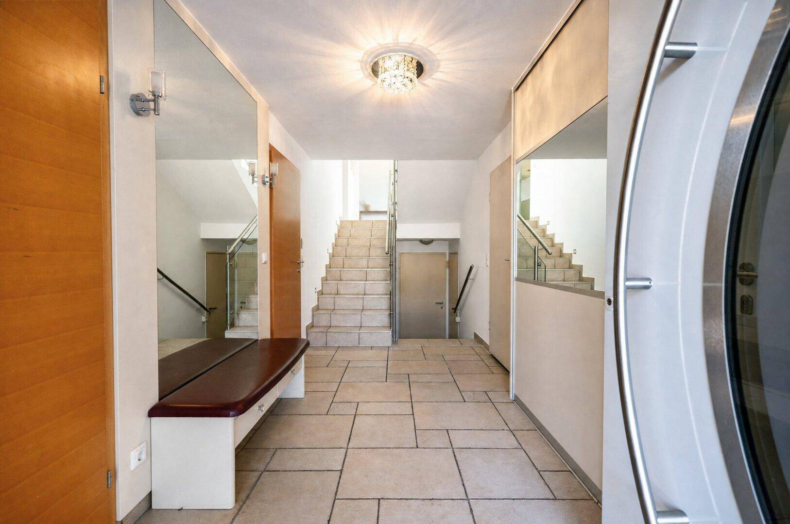 Heller Eingangsbereich mit Fliesenboden, Spiegeln und Treppe zum Obergeschoss.