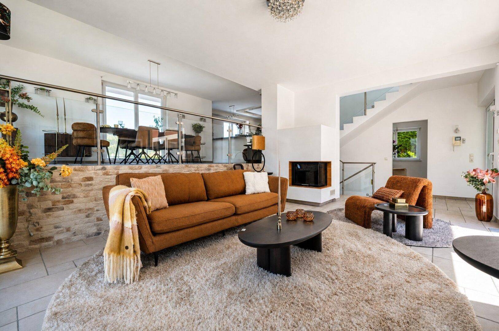 Geräumiges Wohnzimmer mit Kamin, braunem Sofa und offenem Übergang zum Essbereich.